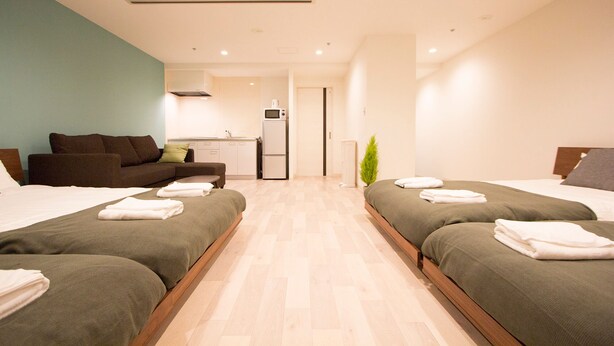 Une chambre d’hôtel avec deux lits, un coin cuisine, un canapé et une petite plante.