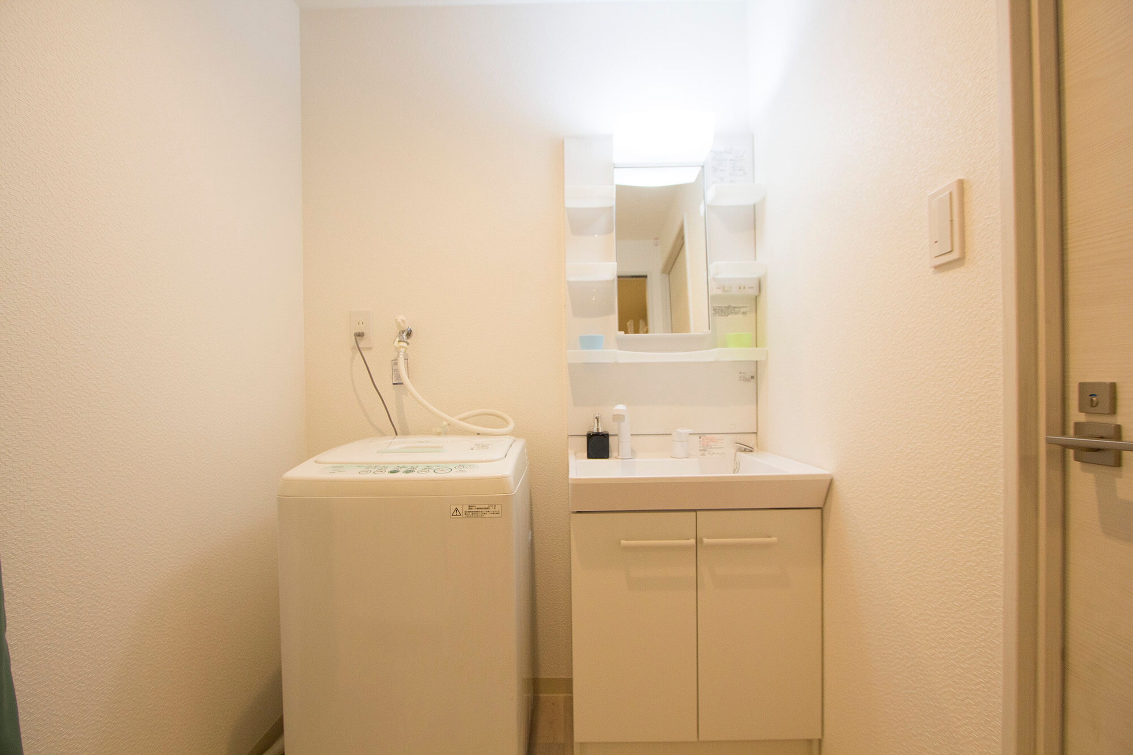 Une petite salle de bain compacte équipée d’un lave-linge, d’un évier et d’un miroir.
