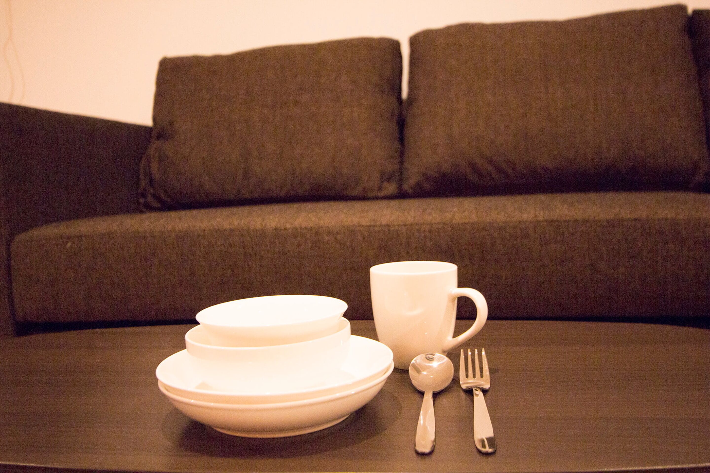 Una mesa con platos, una taza y cubiertos frente a un sofá.