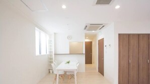 Una habitación luminosa y moderna con suelo de madera, una mesa blanca con sillas, una planta pequeña y un armario.
