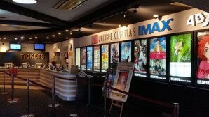 Un mostrador de venta de entradas de cine con la marca IMAX y carteles de películas.