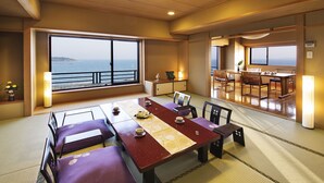 Una habitación tradicional japonesa con suelo de tatami, una mesa baja con cojines y vistas al mar a través de amplias ventanas.
