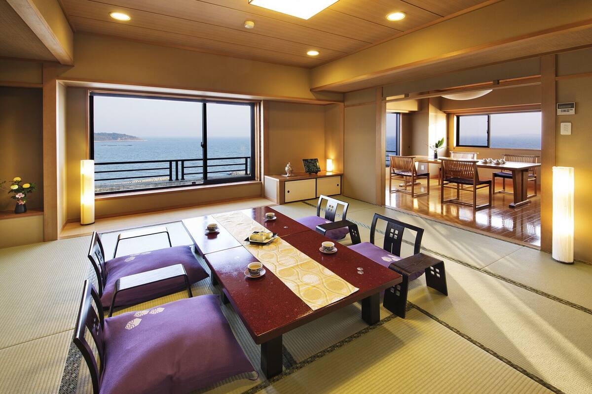 Une pièce de style japonais traditionnel, avec un sol recouvert de tatamis, une table basse avec des coussins et une vue sur la mer grâce à de grandes fenêtres.