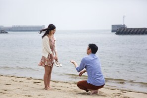 A man kneeling on a beach, proposing to a woman with a ring. - Ryuguhotel KIRA (Nishio)