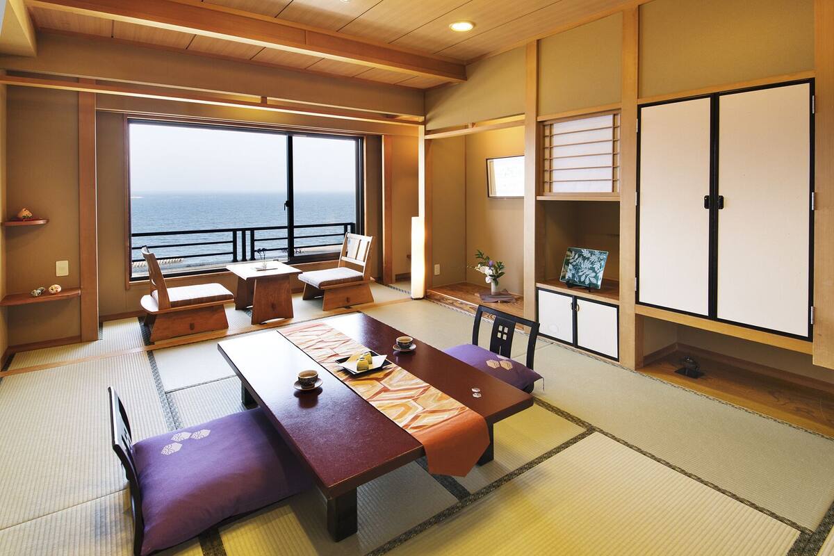Une pièce de style japonais traditionnel, avec un sol recouvert de tatamis, une table basse avec des coussins et une vue sur la mer grâce à de grandes fenêtres.