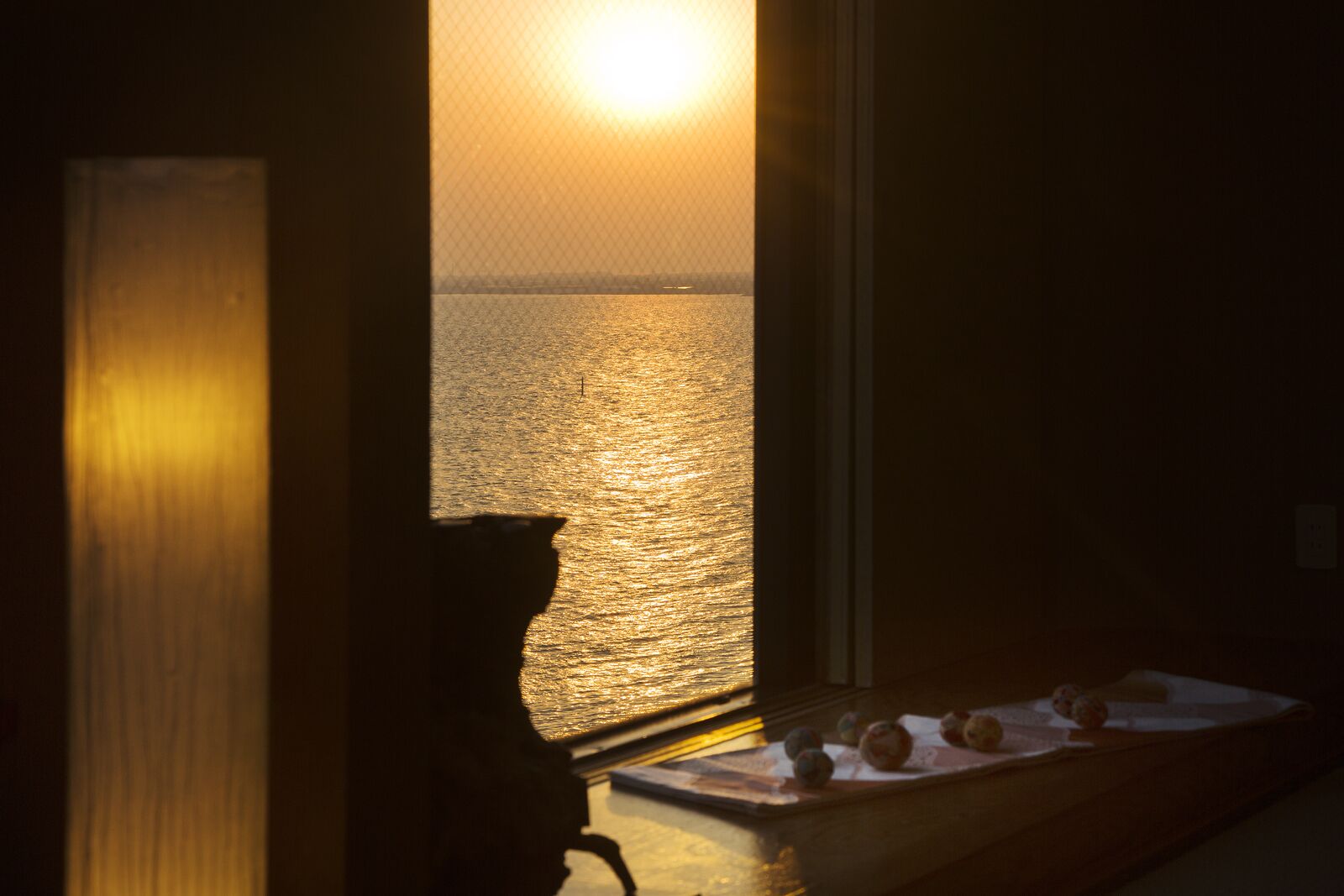 Una habitación con vista al océano al atardecer, un alféizar con una bandeja de manzanas y una silla.