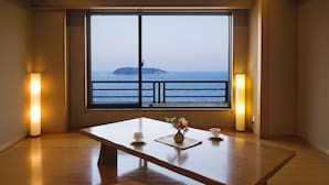 Una habitación con un ventanal grande que da al mar, una mesa de madera con dos tazas y un jarrón de flores, y dos lámparas de pie.