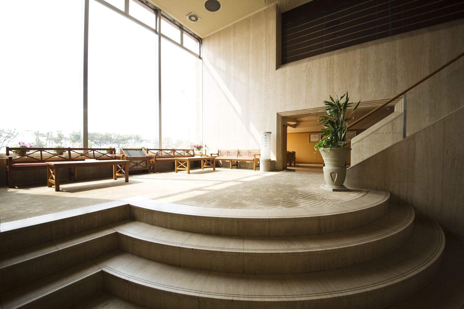 Un interior espacioso con una escalera central, bancos de madera y una planta grande en maceta.