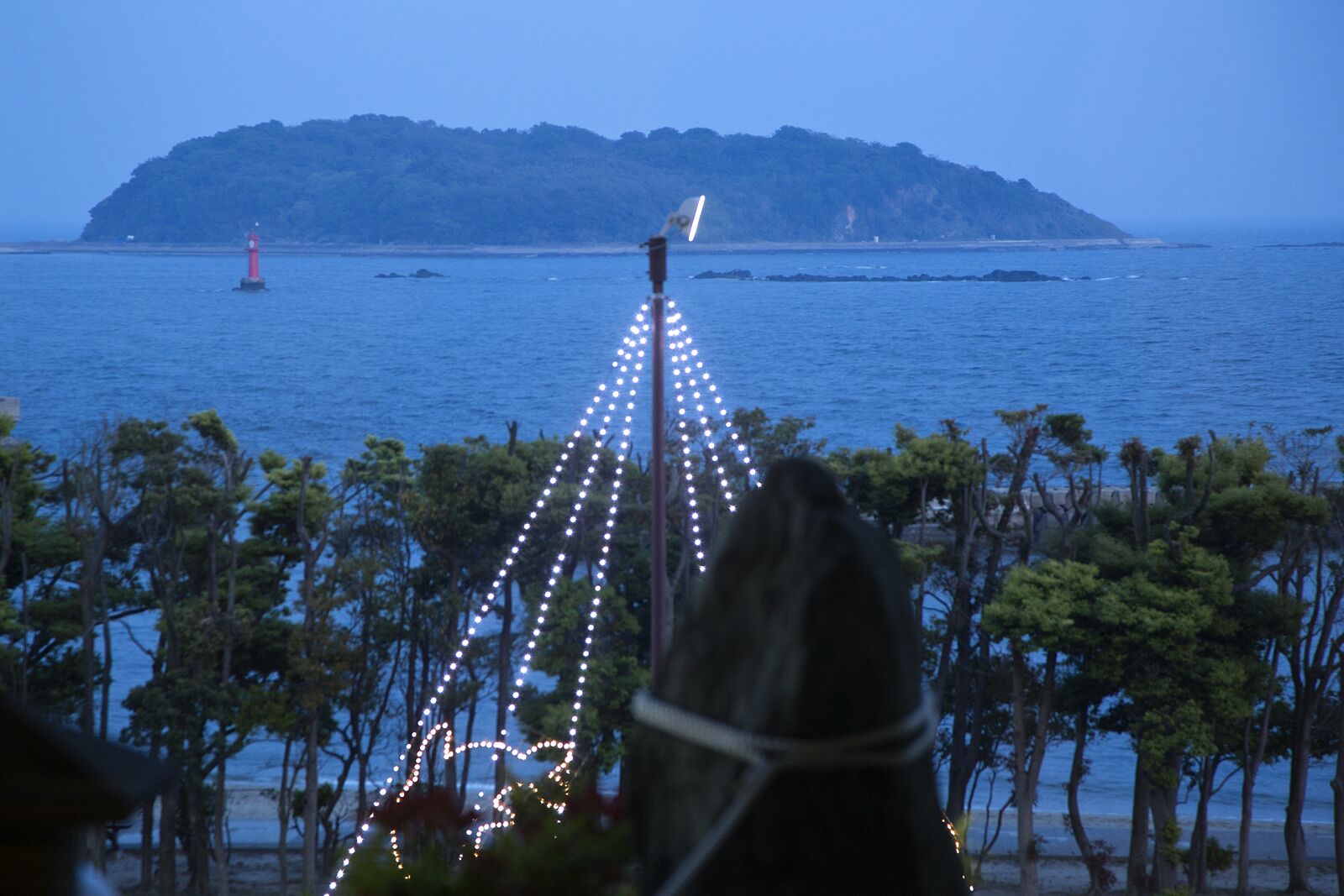 Une vue côtière avec un phare, des arbres et une île au loin.