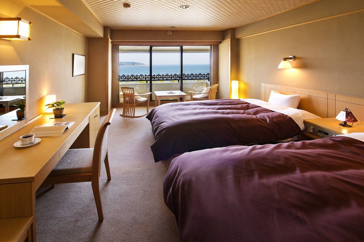 Une chambre d’hôtel avec deux lits, un bureau avec une chaise, une petite table et un balcon donnant sur la mer.