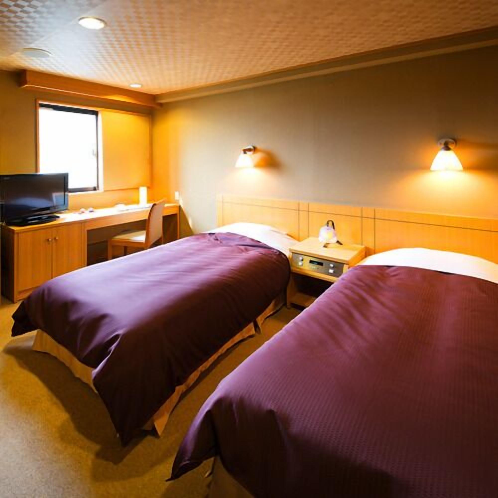 Une chambre d’hôtel avec deux lits, un bureau avec un ordinateur et une fenêtre.