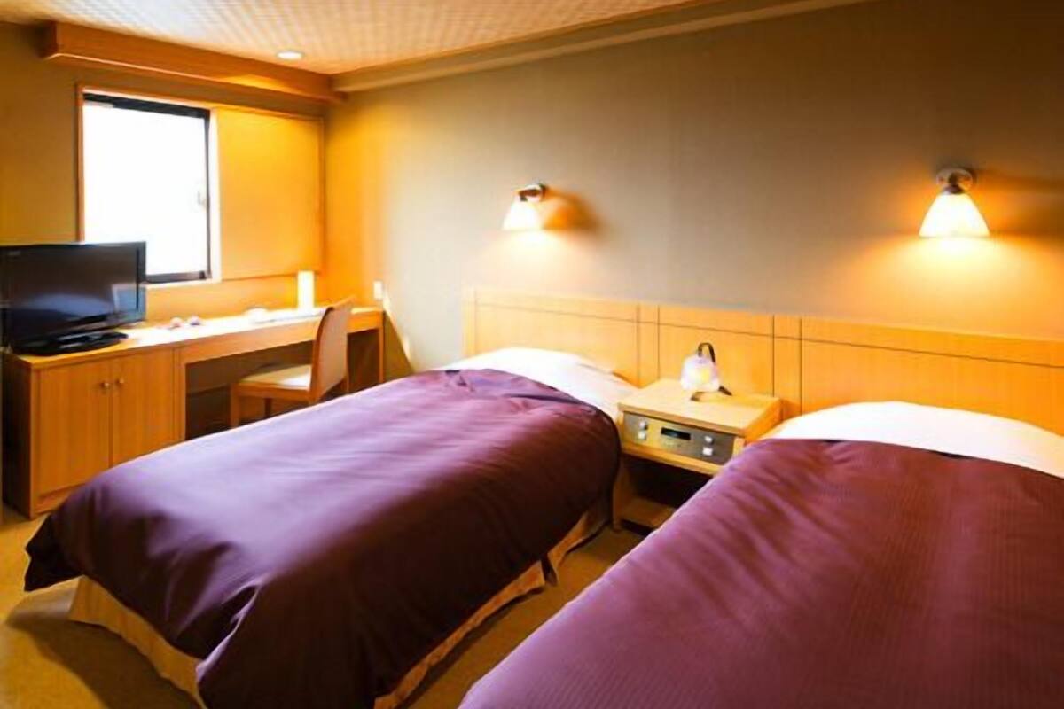 Une chambre d’hôtel avec deux lits, un bureau avec un ordinateur et une fenêtre.