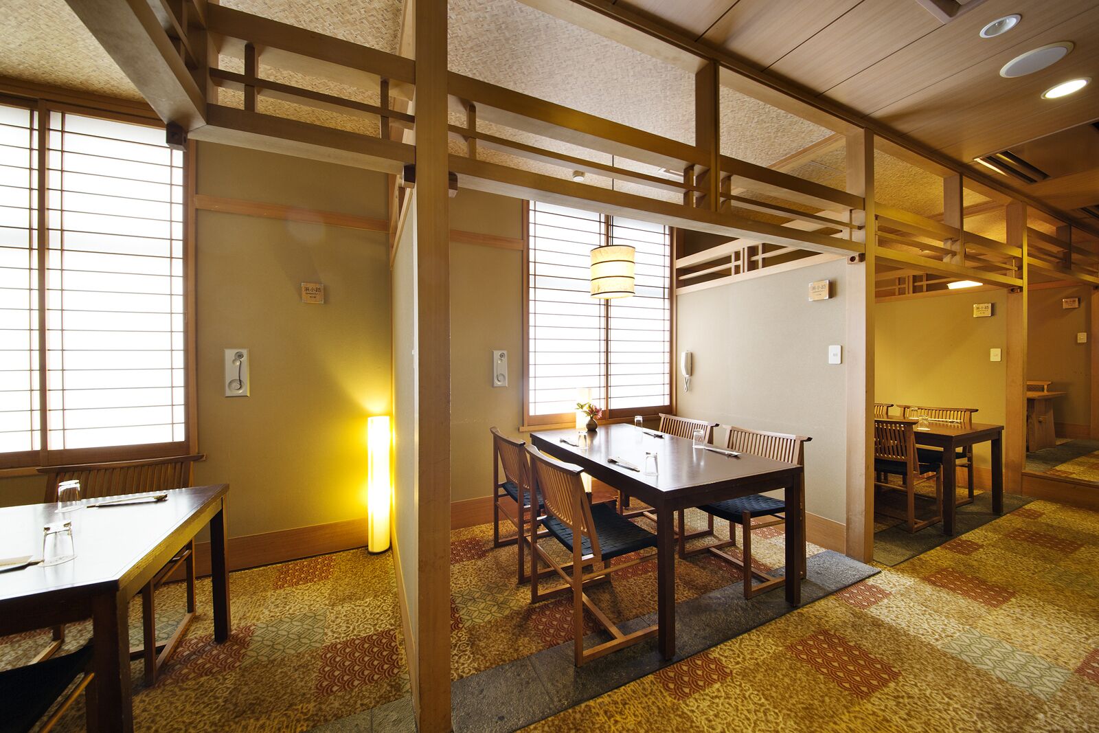 Une pièce de style japonais traditionnel, avec un sol recouvert de tatamis, une table basse et des chaises, ainsi que des portes coulissantes.