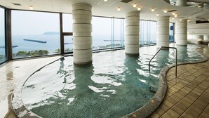 Una amplia piscina interior con vista al mar, rodeada de columnas y ventanas grandes.