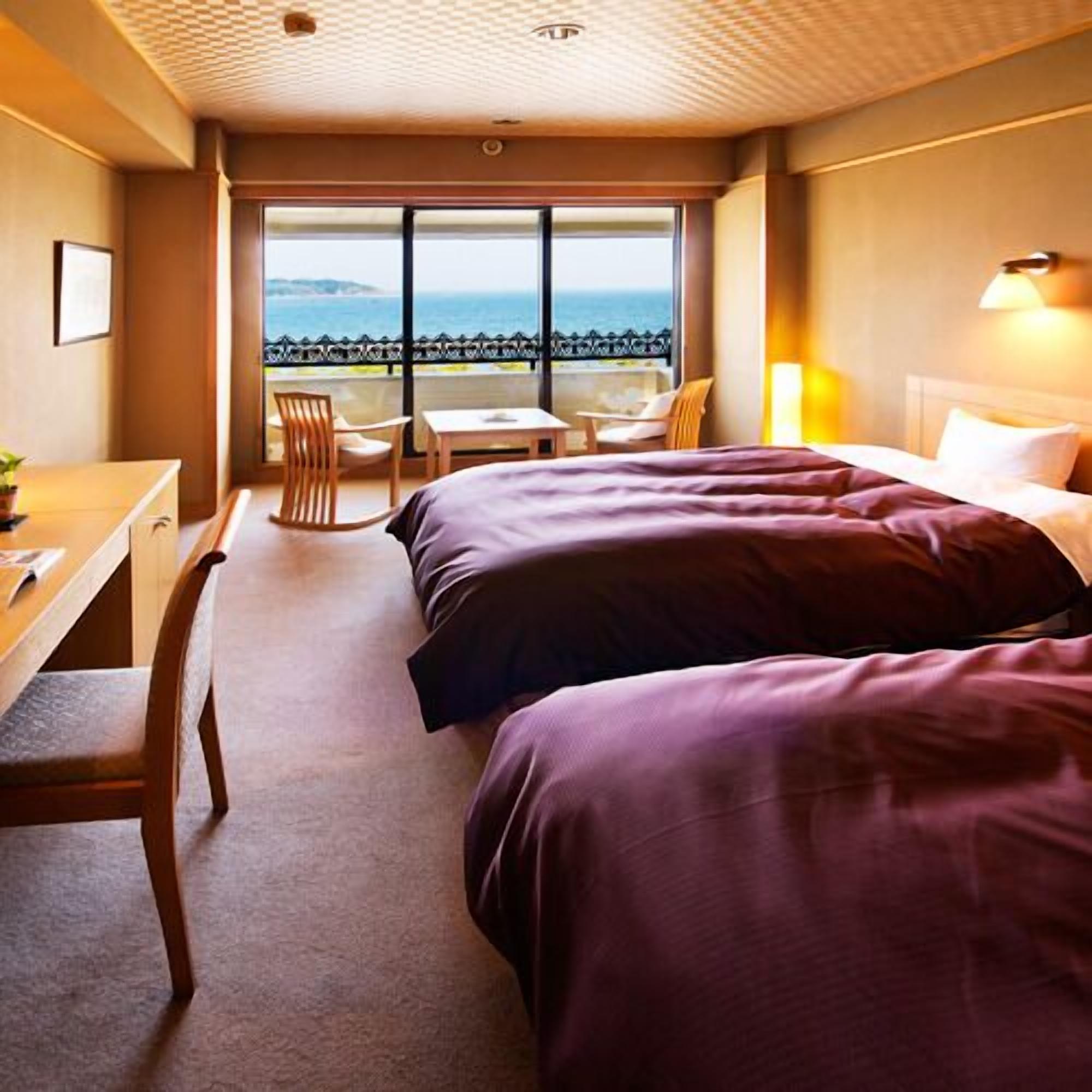 Une chambre d’hôtel avec deux lits, un bureau, une chaise et une vue sur la mer.
