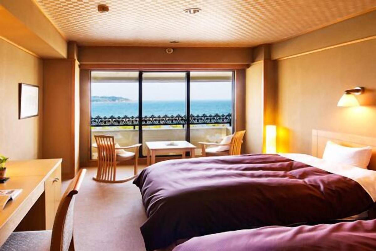 Une chambre d’hôtel avec deux lits, un bureau, une chaise et une vue sur la mer.