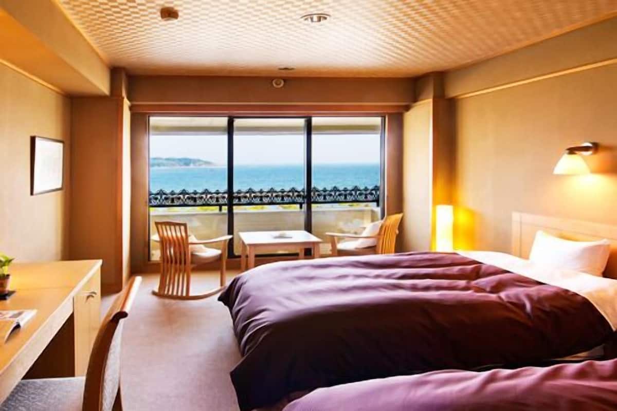 Une chambre d’hôtel avec deux lits, un bureau, une chaise et une vue sur la mer.