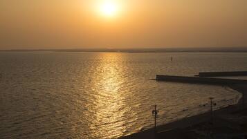 A coastal sunset with a calm sea reflecting the sun, a pier extending into the water, and a distant shoreline.