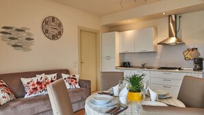 En moderne stue med sofa, spisebord og køkken i baggrunden.