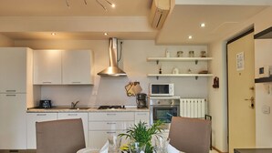 Et moderne køkken med hvide skabe, et rustfrit stål emfang, en mikroovn og en indbygget ovn. Der er et spisebord dækket med tallerkener, glas og en vase med blomster.