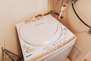Una lavadora Toshiba blanca con panel de control y manguera de entrada de agua.