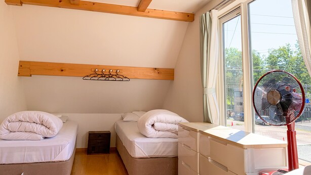 A room with two beds, a wooden ceiling, a window with a view, and a red fan. - Trailside Apartments & Chalet (Kutchan)
