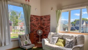 A cozy room with a brick accent wall, a white sofa with cushions, a small armchair, and a standing fan. - Trailside Apartments & Chalet (Kutchan)