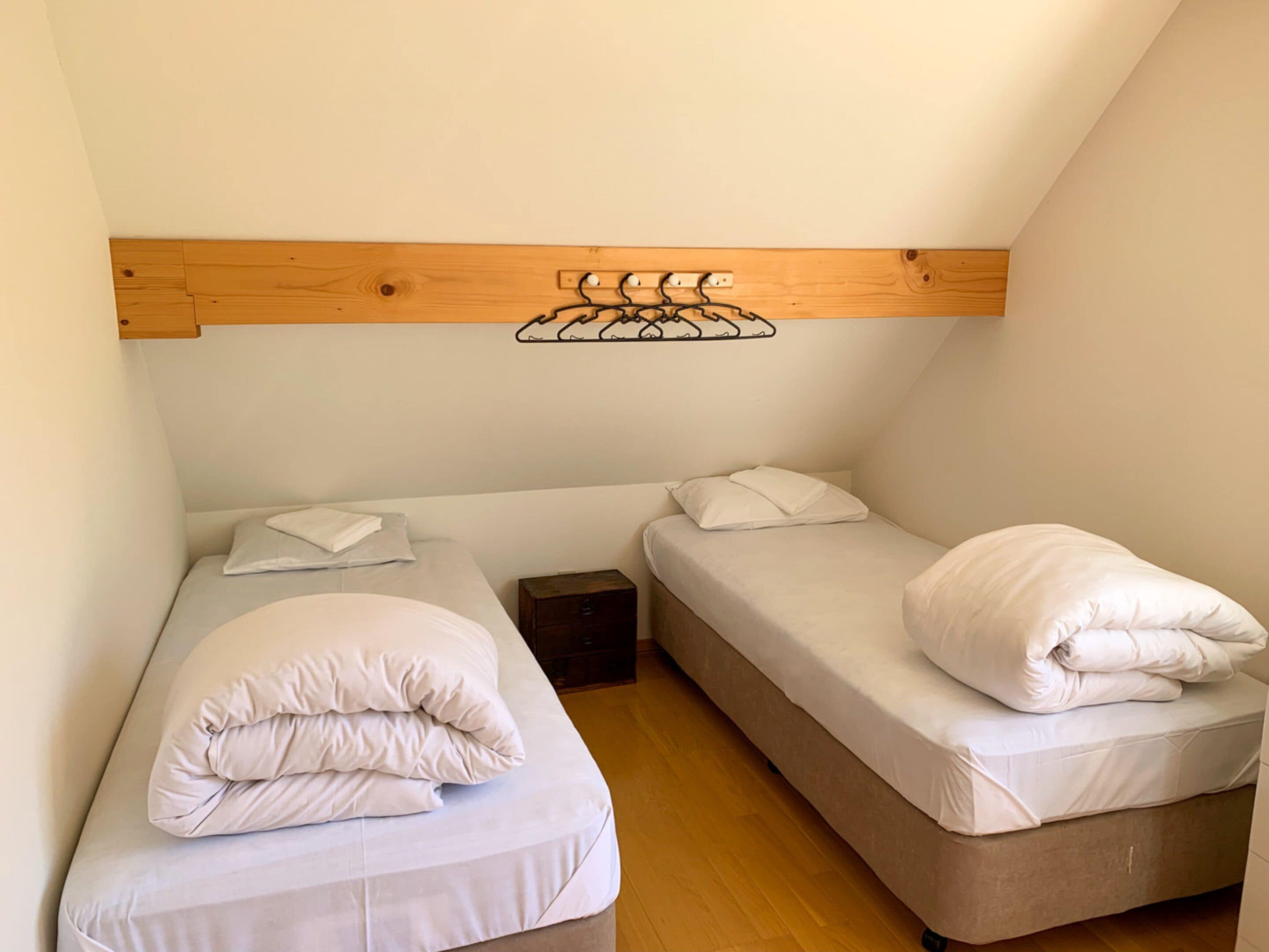 A small, compact room with two single beds, a wooden ceiling, and a simple wall-mounted shelf.