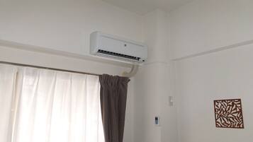 Une pièce dans laquelle un climatiseur blanc est fixé au mur, au-dessus d’une fenêtre ornée de rideaux blancs et légers.