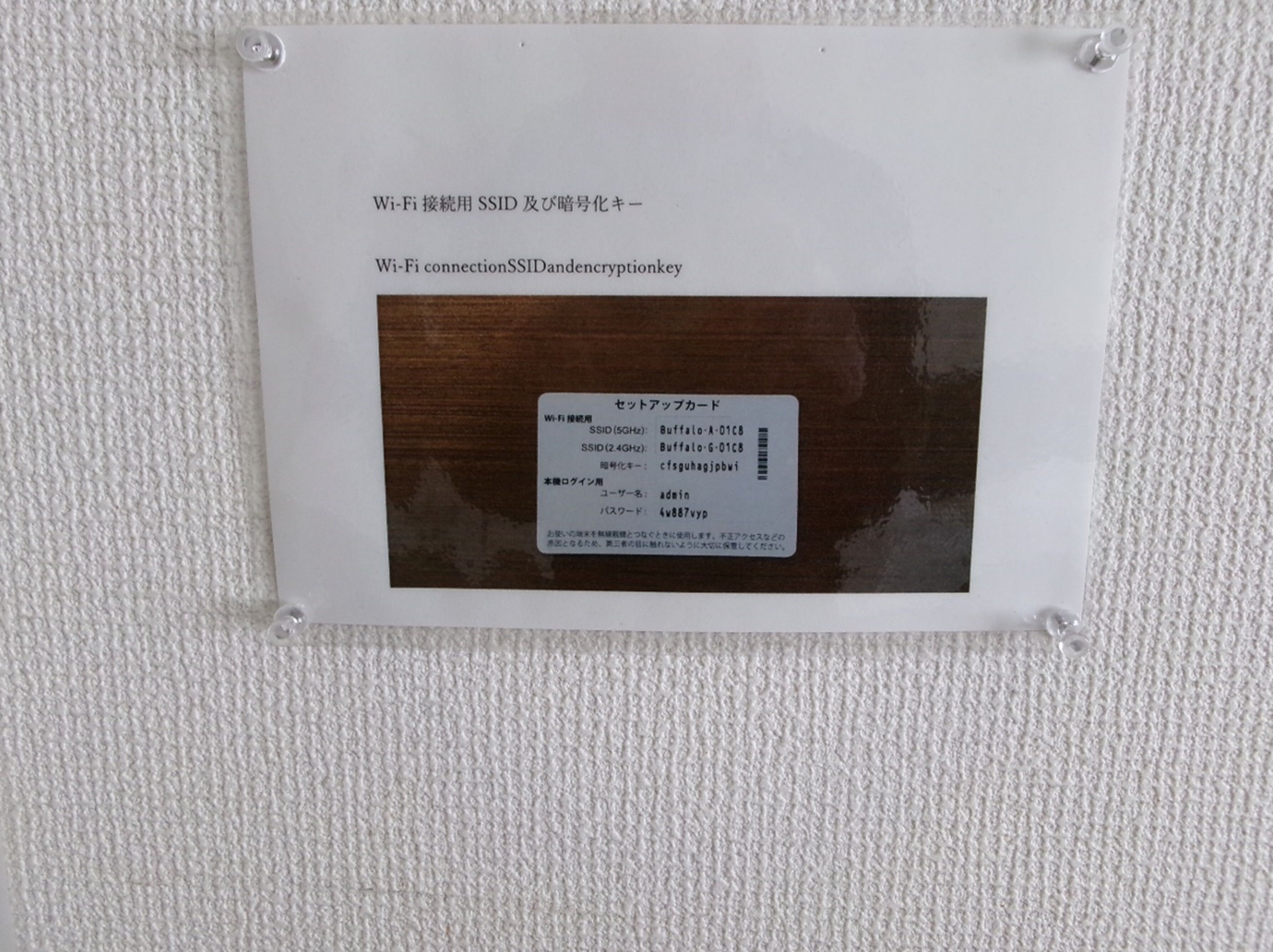 A sign with Japanese text and a barcode, mounted on a textured wall.