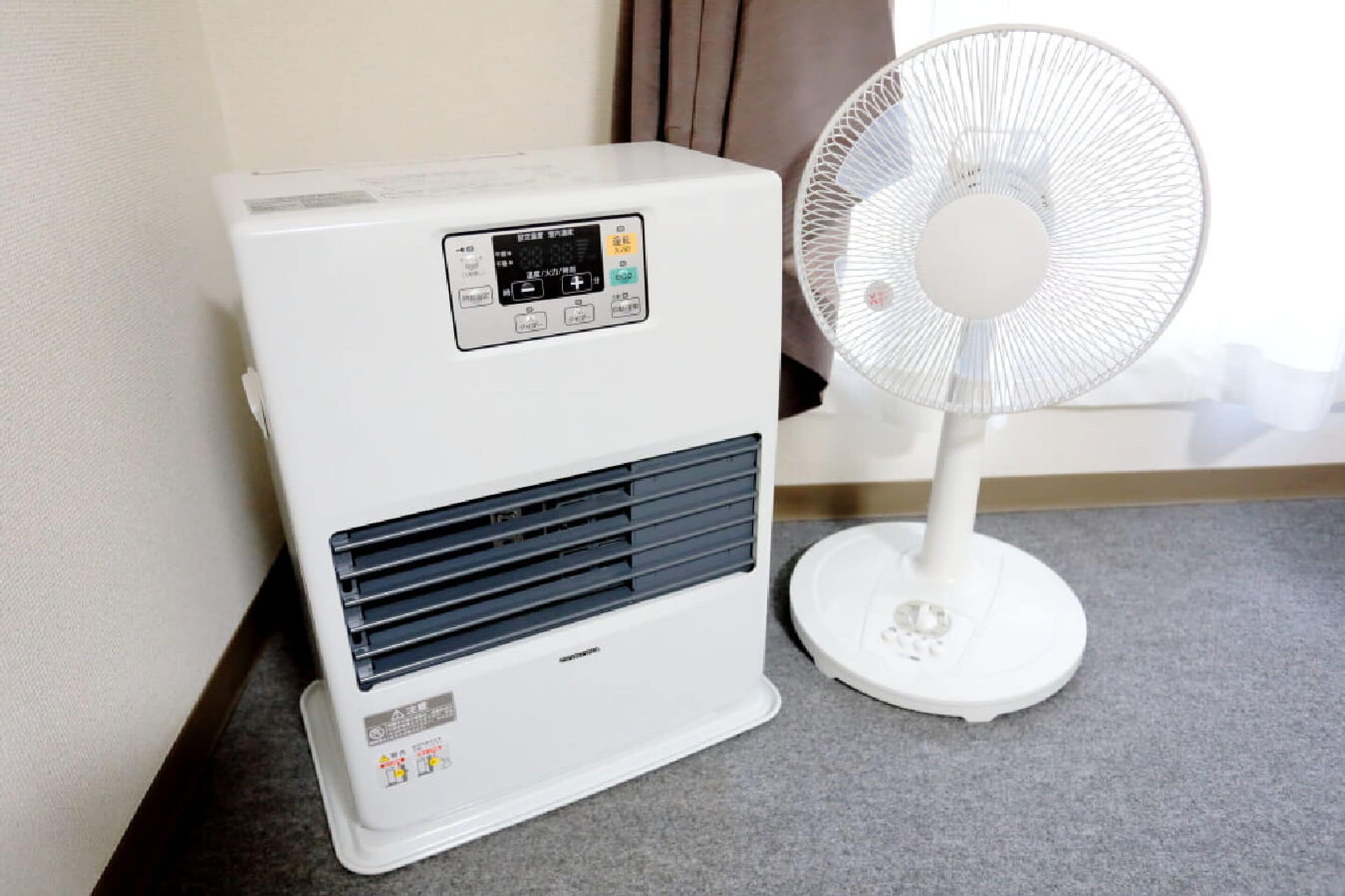 Un aire acondicionado portátil blanco con pantalla digital y un ventilador de pie blanco a su lado.
