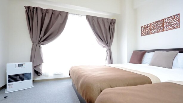 A hotel room with a bed, a bedside table, a wall-mounted air conditioner, and a window with curtains.