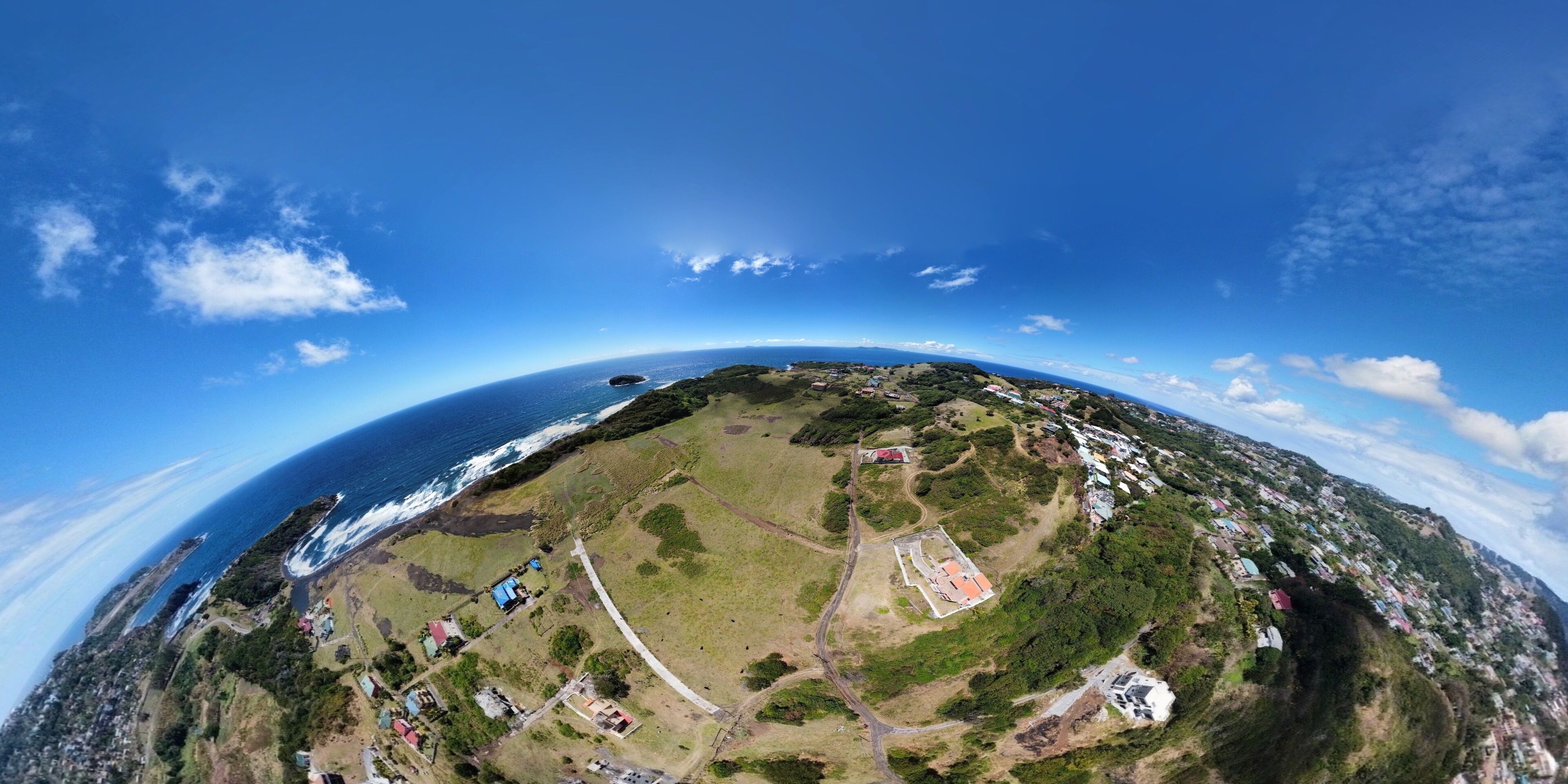 A panoramic view of a coastal area with a clear sky, a winding road, and scattered buildings.