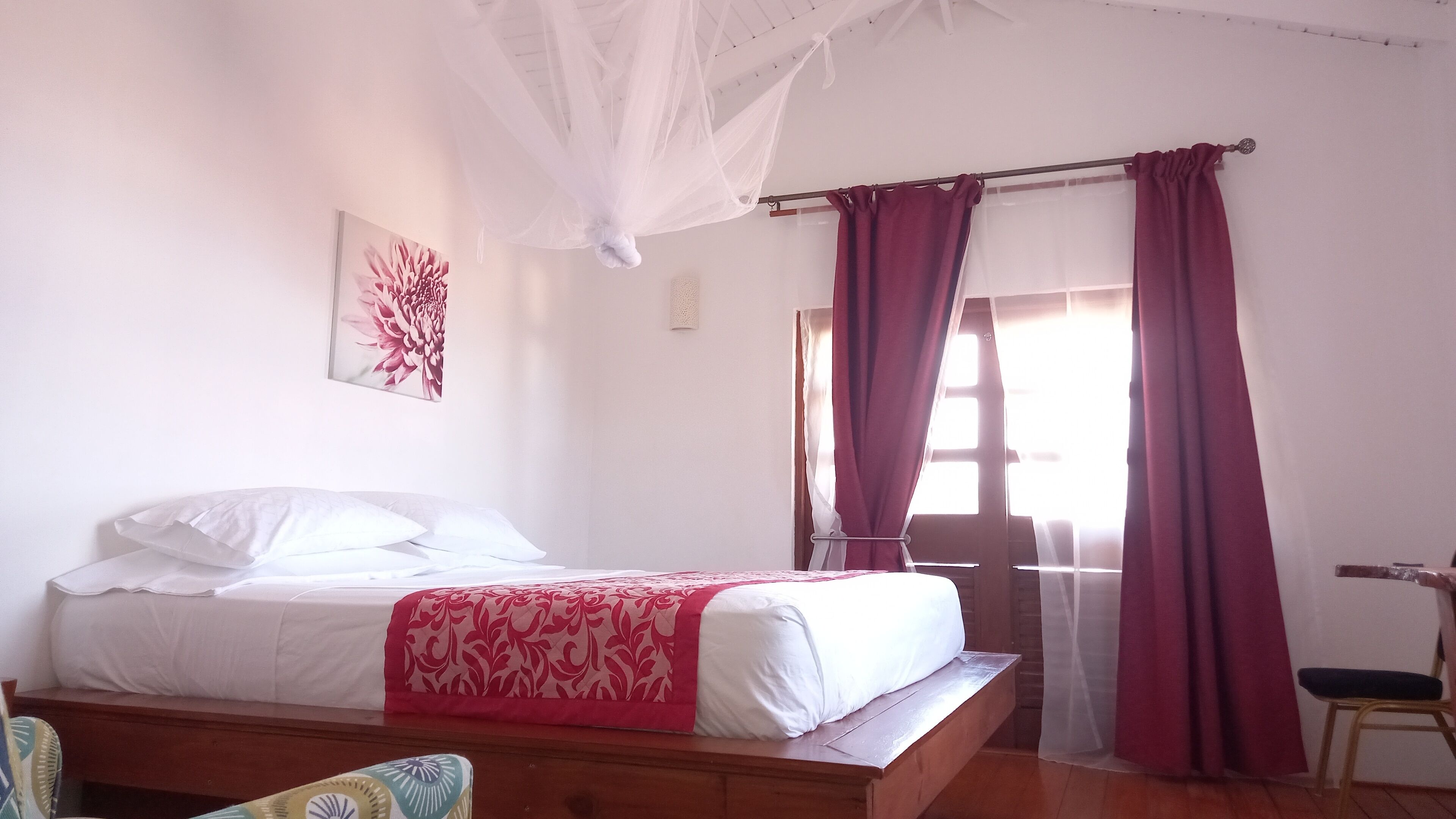 Un dormitorio con una cama, una silla, una ventana con cortinas y una obra de arte colgada en la pared.