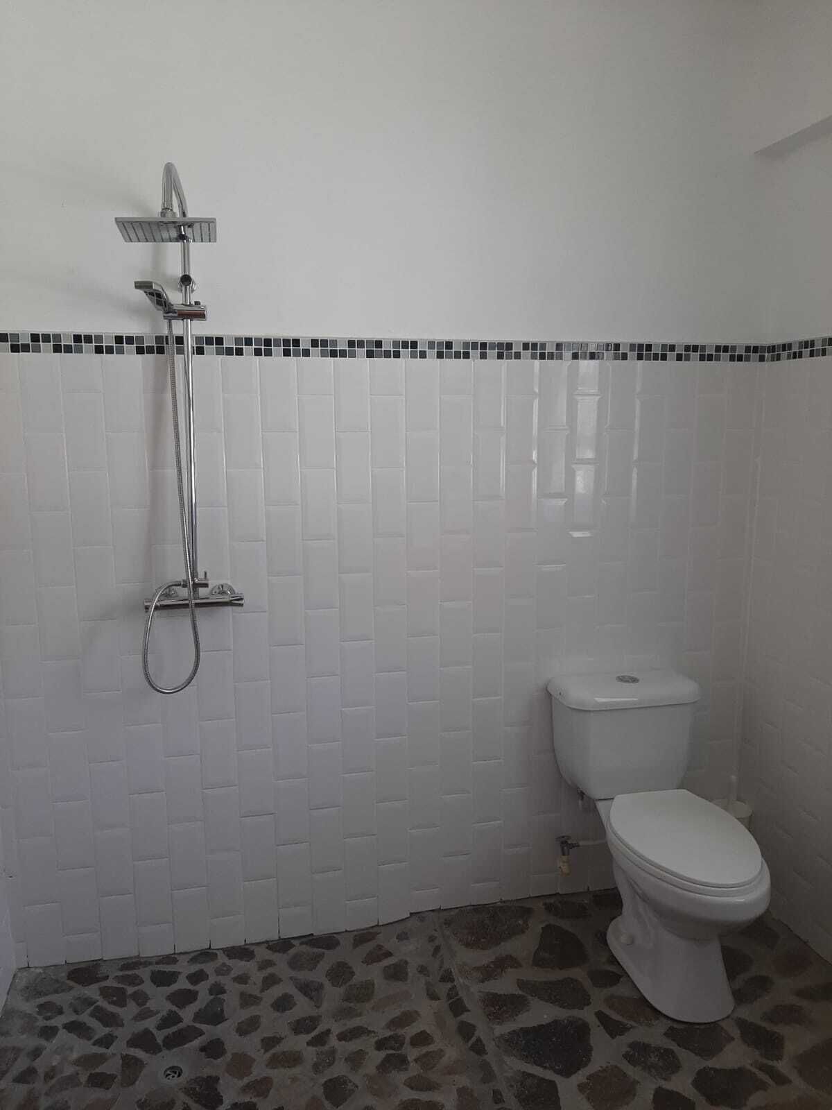 A bathroom with white tiled walls, a shower, and a toilet.