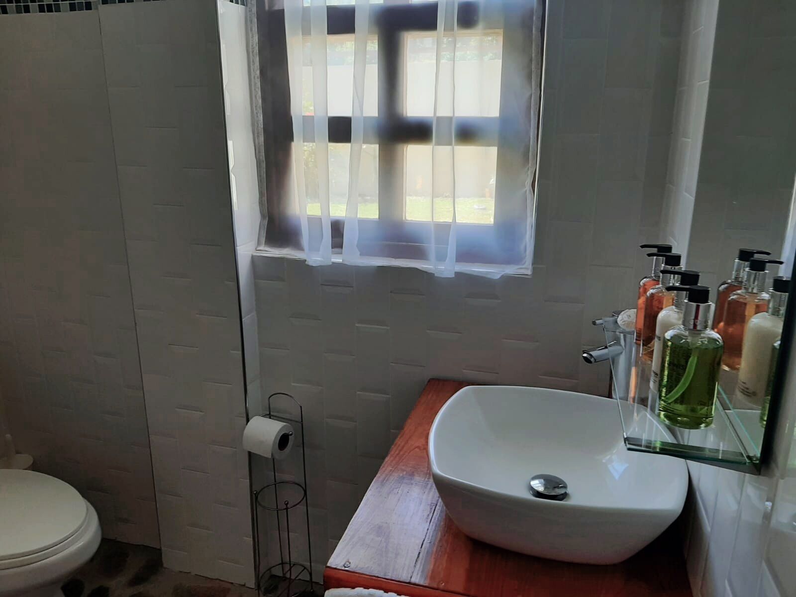 A bathroom with a white toilet, a wooden vanity, a white sink with a mirror, and toiletries on the counter.