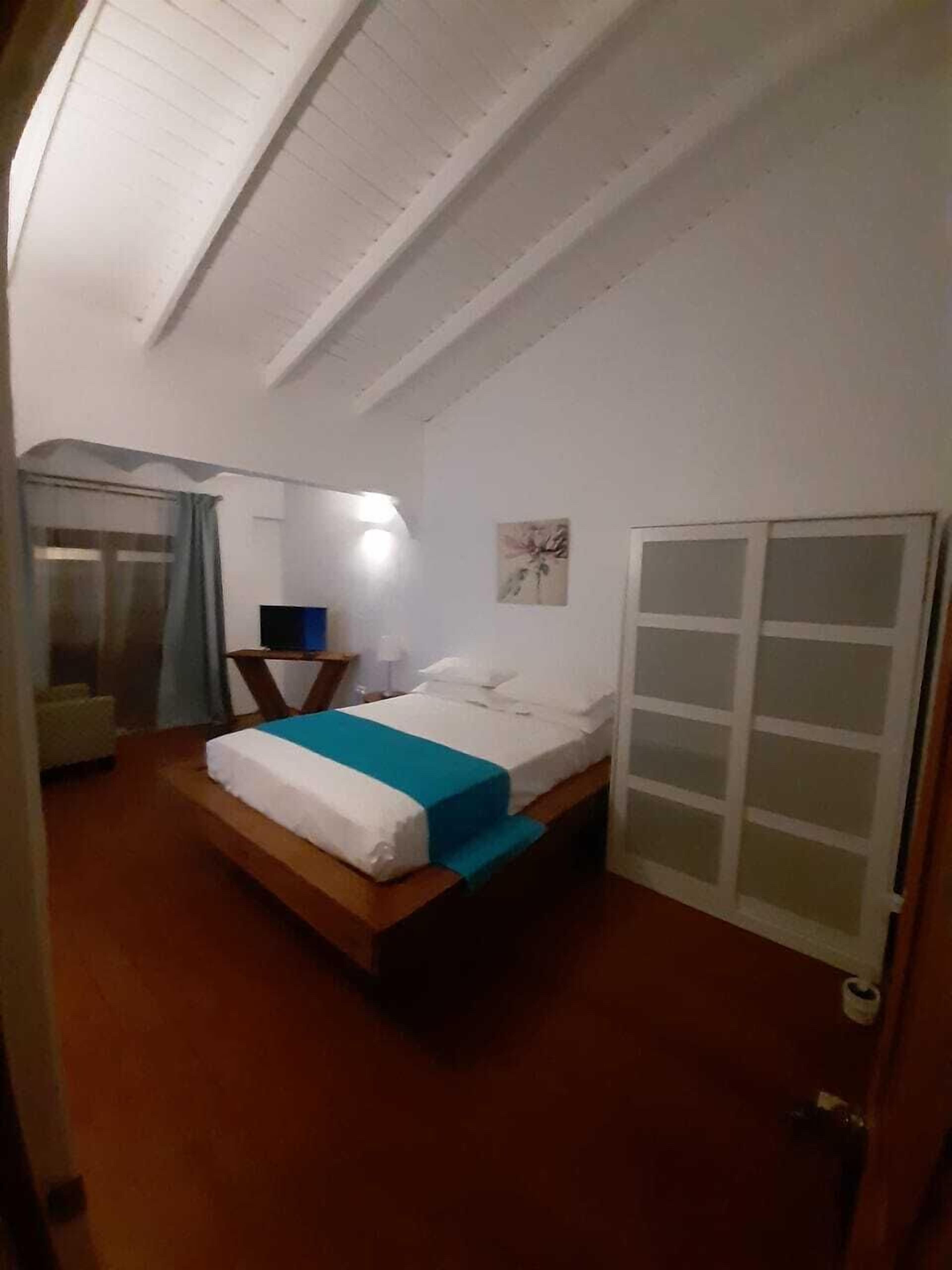 A bedroom with a bed, a nightstand, a desk, a chair, a window with curtains, and a door.