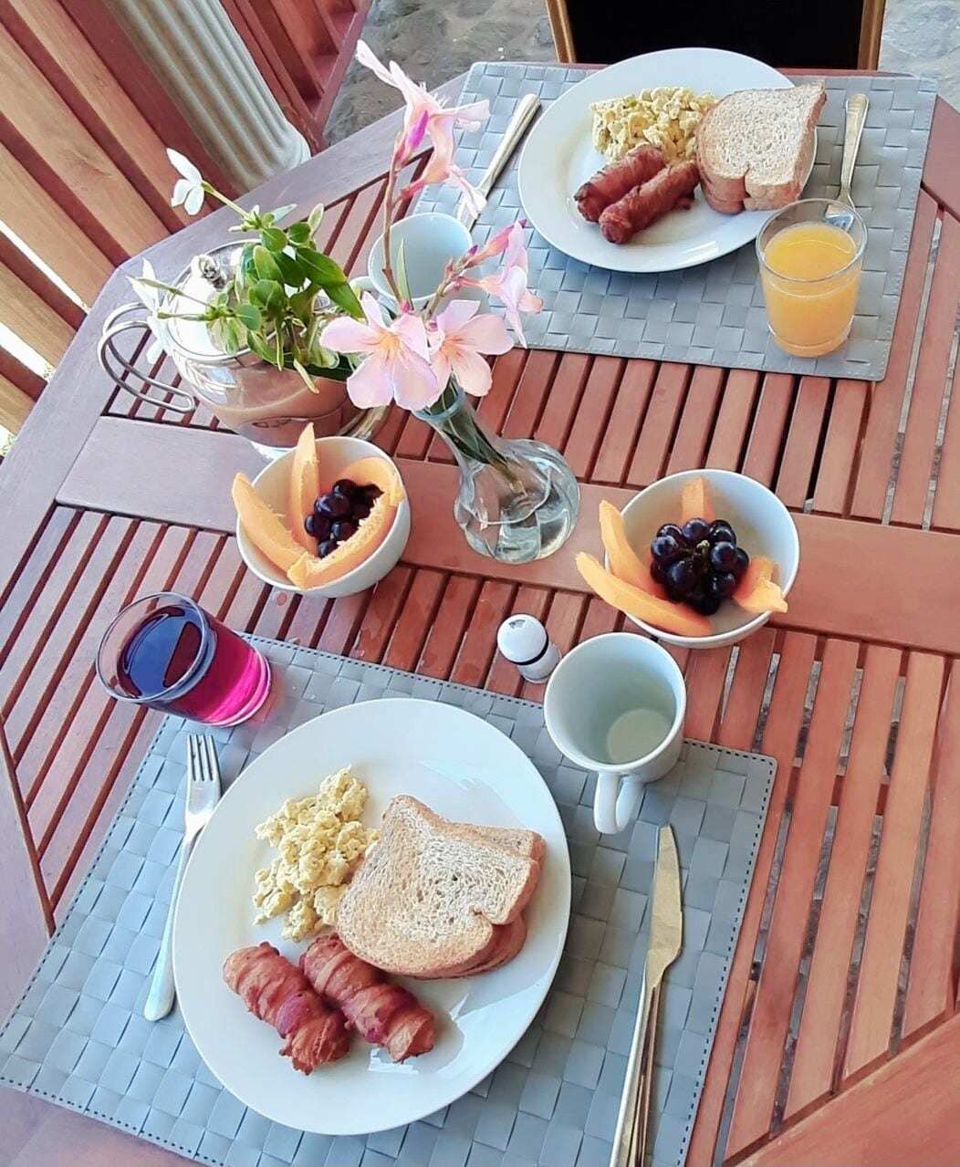 Desayuno con platos de huevos, tocino, tostadas y fruta sobre una mesa de madera.