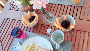 Desayuno con platos de huevos, tocino, tostadas y fruta sobre una mesa de madera.