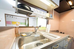 A kitchen with a stainless steel sink, a dish rack, and a shelf above the sink holding plates and bowls. - Stay inn FREE (Sapporo)