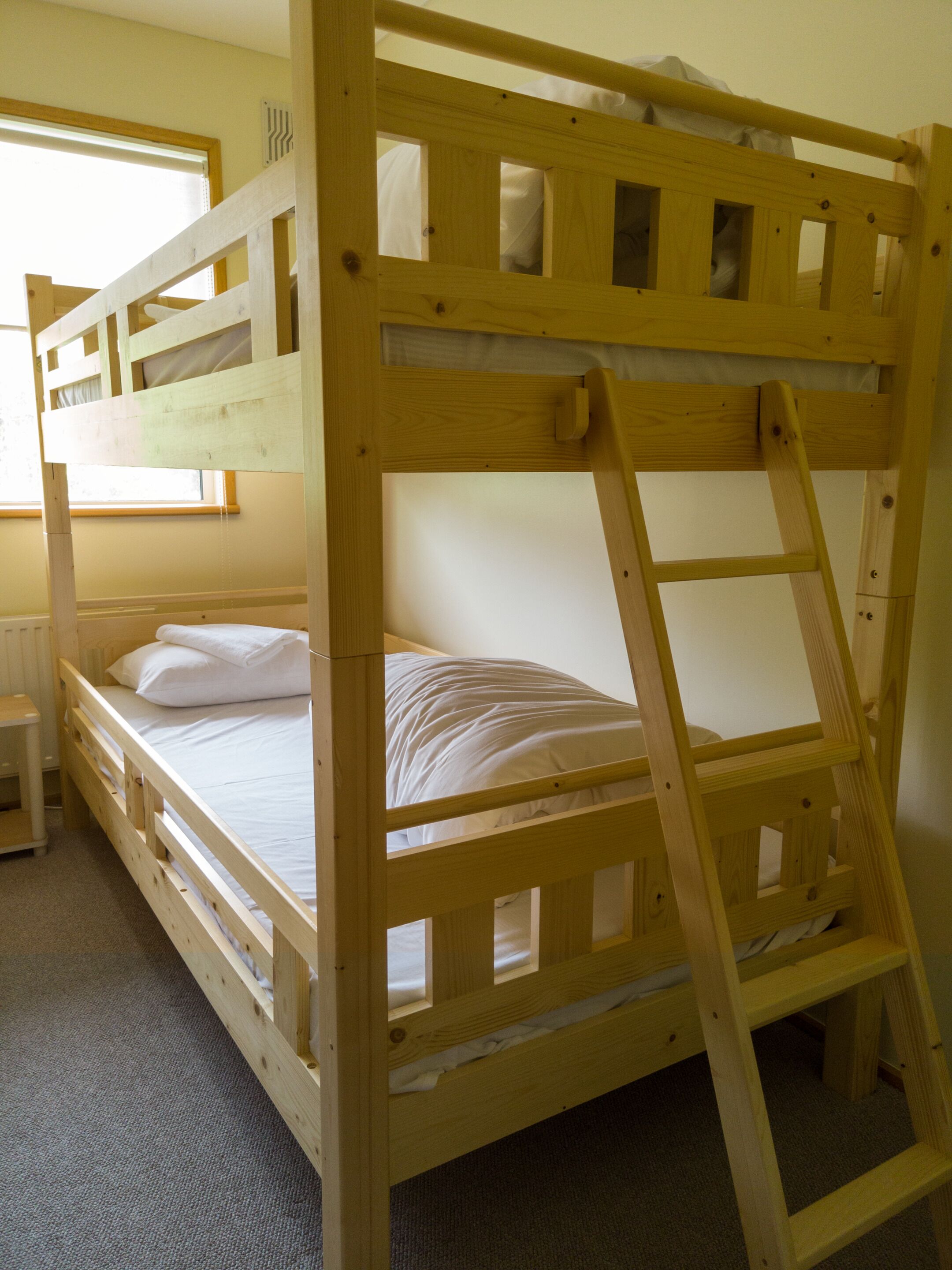 Una litera con escalera, una mesita de noche y una ventana con persianas.