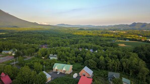 Paisagem rural com casas dispersas, rodeada por florestas densas e montanhas ao fundo.