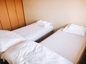 Two single beds with white linens and pillows, a wooden wardrobe, and a plain wall. - Yotei Town House (Niseko)