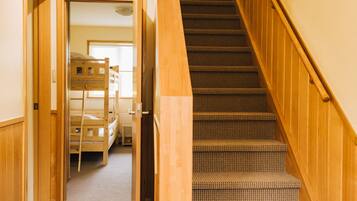 Una escalera con barandillas de madera y peldaños alfombrados que conduce a una habitación con literas.