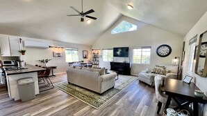 A spacious living area with a high ceiling, a ceiling fan, a dining area with a table and chairs, a kitchen with appliances, and a large window providing natural light. - Barn house stay near Palisade, hot tub and views! (Clifton)