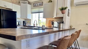 A modern kitchen with white cabinets, a black refrigerator, a wooden countertop, and a sign that says "let's eat". - Barn house stay near Palisade, hot tub and views! (Clifton)