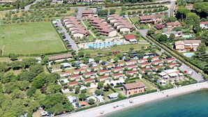 Eine Luftaufnahme eines Küstenresorts mit mehreren bungalowartigen Unterkünften, einem zentralen Poolbereich und einem Strand.