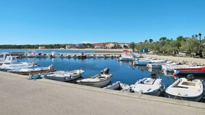 A marina with various small boats docked, a clear blue sky, and buildings in the background.