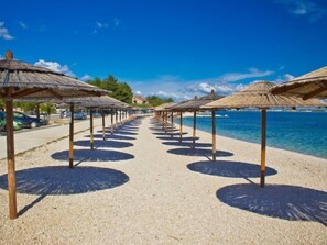 A beach with rows of thatched umbrellas and a clear view of the ocean. - Apartment Fliri by Interhome (Vir)