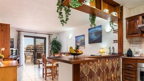 Een moderne keuken met houten kastjes, een centraal kookeiland met een fruitschaal, en uitzicht naar buiten.